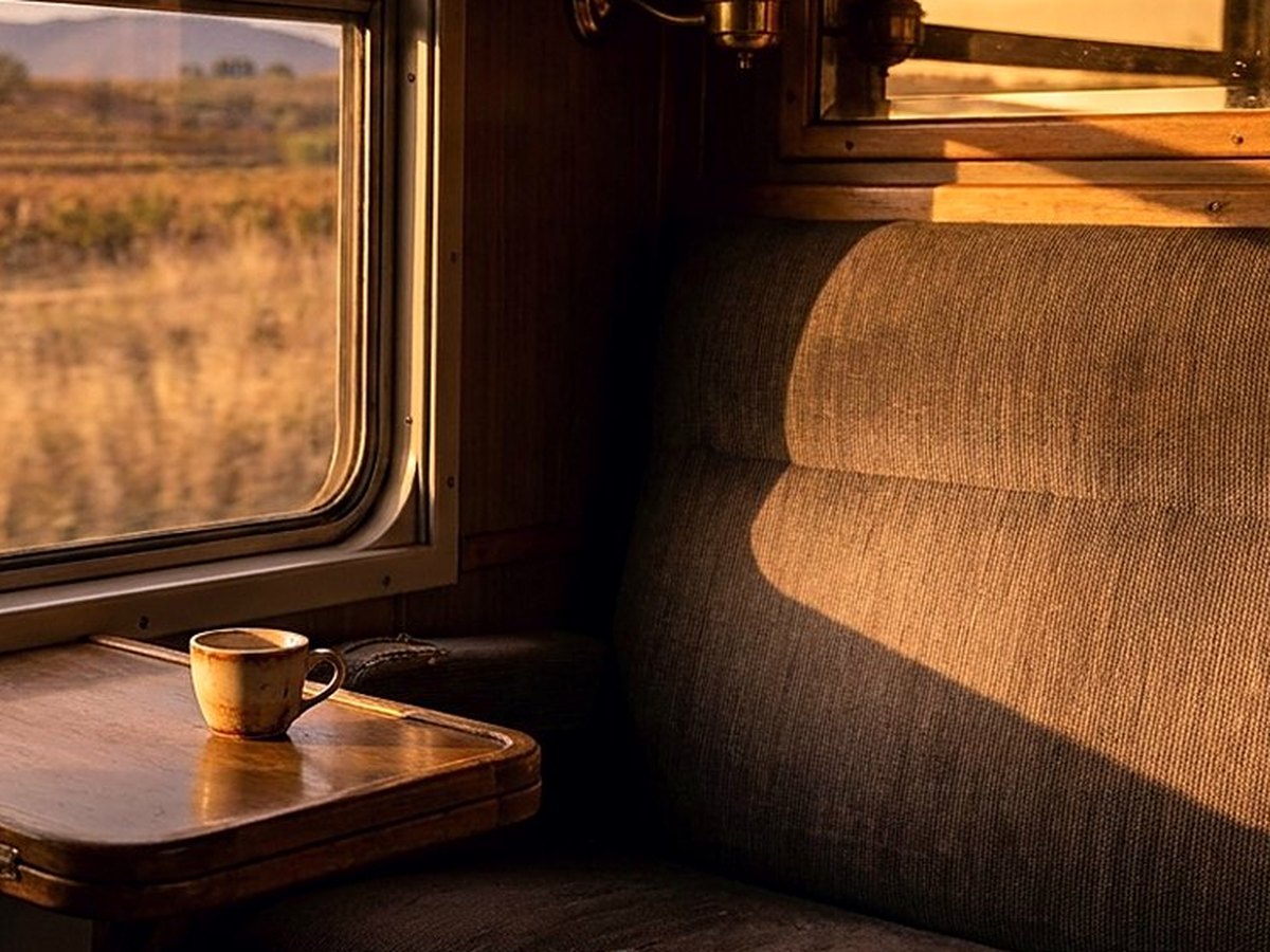 View from a train window of green hills and a lake in low afternoon sun, a folded jacket on the seat beside the glass